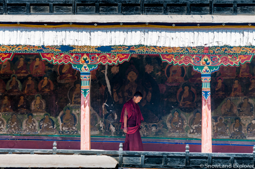 A monk is walking in front of old wall paintings in Tashilhunpo Monastery in Shigatse